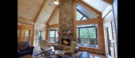 Cozy lodge room with a stone fireplace, comfortable seating, and a large window offering a forest view.