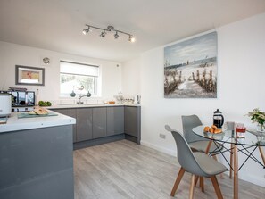 Una cocina moderna con armarios grises, un comedor con mesa de vidrio y un cuadro de una playa en la pared.