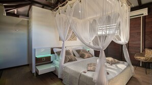A bedroom with a canopy bed, bedside tables, and a chair. - Fleur de Canne (Le Diamant)