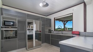 A modern kitchen with built-in appliances, a large window, and a view of the outdoors. - Fleur de Canne (Le Diamant)