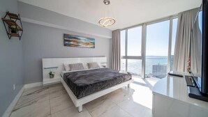 Camera moderna con un letto grande, un quadro, vista sulla città e un balcone con tende.