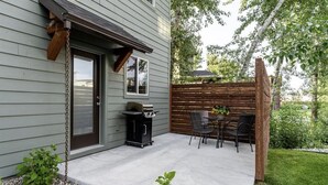 A covered patio with a grill, outdoor seating, and a wooden fence. - Rainbow Haven down by the Gallatin River (Bozeman)