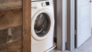 A stacked washer and dryer unit in a hallway with a wooden accent wall. - Rainbow Haven down by the Gallatin River (Bozeman)