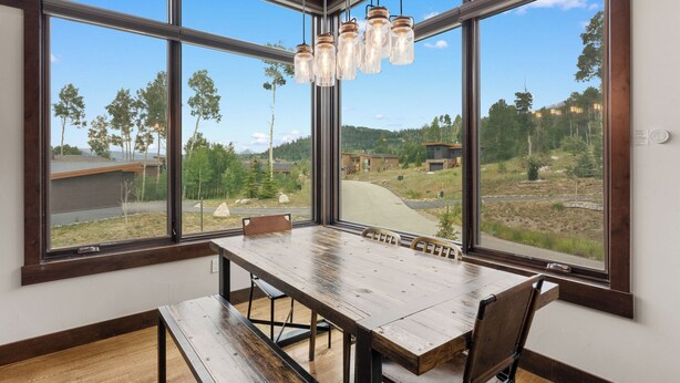 A dining area with a large wooden table and chairs, large windows with a view of a forest and buildings. - 15 W Benjamin Lane by Summit County Mountain Retreats (Silverthorne)