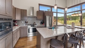 A modern kitchen with granite countertops, stainless steel appliances, and large windows offering a view of the outdoors. - 15 W Benjamin Lane by Summit County Mountain Retreats (Silverthorne)