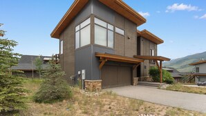 A modern two-story house with a large garage, a covered porch, and a view of the surrounding landscape. - 15 W Benjamin Lane by Summit County Mountain Retreats (Silverthorne)