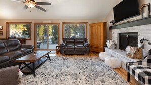 A spacious living room with a fireplace, leather sofa, and a large TV. - 8 Crown Drive by Summit County Mountain Retreats (Breckenridge)