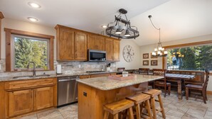 A kitchen with wooden cabinets, a granite countertop, a stainless steel dishwasher, and a bar area with stools. - 8 Crown Drive by Summit County Mountain Retreats (Breckenridge)