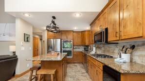 A modern kitchen with wooden cabinets, granite countertops, stainless steel appliances, and a bar area. - 8 Crown Drive by Summit County Mountain Retreats (Breckenridge)