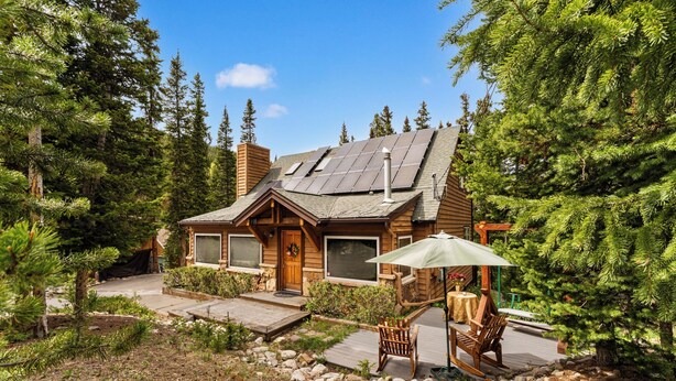 A log cabin with a deck, surrounded by trees.