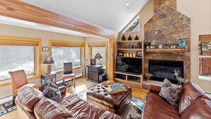 A cozy living room with leather sofas, a fireplace, a TV, and a stone wall.