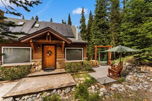 A log cabin with a wooden deck, a porch with chairs, and a view of a forest.
