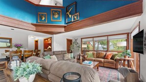 A spacious living room with a large sectional sofa, a dining area with wooden furniture, and a kitchen visible through an open space. - 67 W Hanson Road by Summit County Mountain Retreats (Keystone)