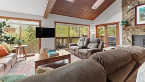 A spacious living room with a high ceiling, large windows, a fireplace, and a cozy seating area. - 67 W Hanson Road by Summit County Mountain Retreats (Keystone)
