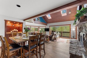 Un amplio comedor con mesas y sillas de madera, una chimenea de piedra y ventanas grandes que ofrecen vistas al exterior.
