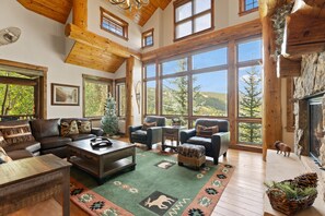 A spacious living room with a large window overlooking a forested landscape, a fireplace, and a cozy seating area.