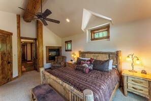 A bedroom with a sloped ceiling, a ceiling fan, a bed with patterned bedding, a nightstand with lamps, and a window with a view. - 227 North Fork Road by Summit County Mountain Retreats (Keystone)