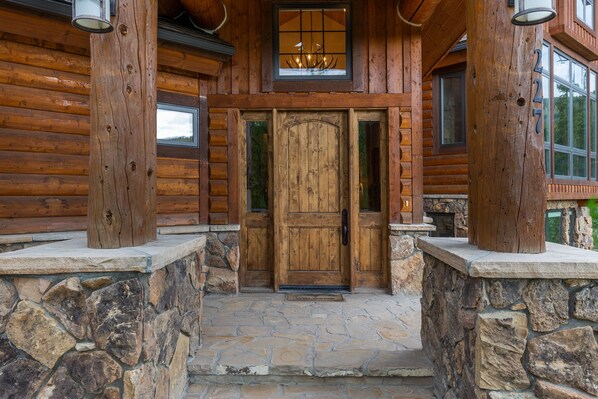 A wooden log cabin with a stone entrance, a wooden door, and a window with a chandelier. - 227 North Fork Road by Summit County Mountain Retreats (Keystone)