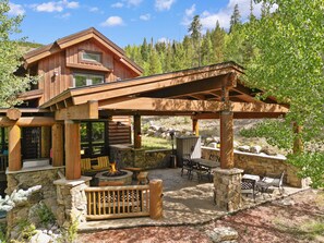 A wooden cabin with a stone fireplace, outdoor seating, and a covered patio area.