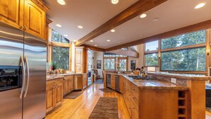 A modern kitchen with wooden cabinets, stainless steel appliances, and large windows offering a view of the outdoors.