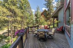 A wooden deck with outdoor furniture, surrounded by trees and a building with a gabled roof. - 580 Elk Circle by Summit County Mountain Retreats (Keystone)