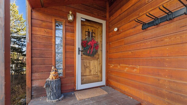 Una cabana de fusta amb una porta d'entrada decorada amb una corona i un llaç vermell. Hi ha una petita estàtua de fusta d'un os per fora de la porta, sobre un penya-segat.