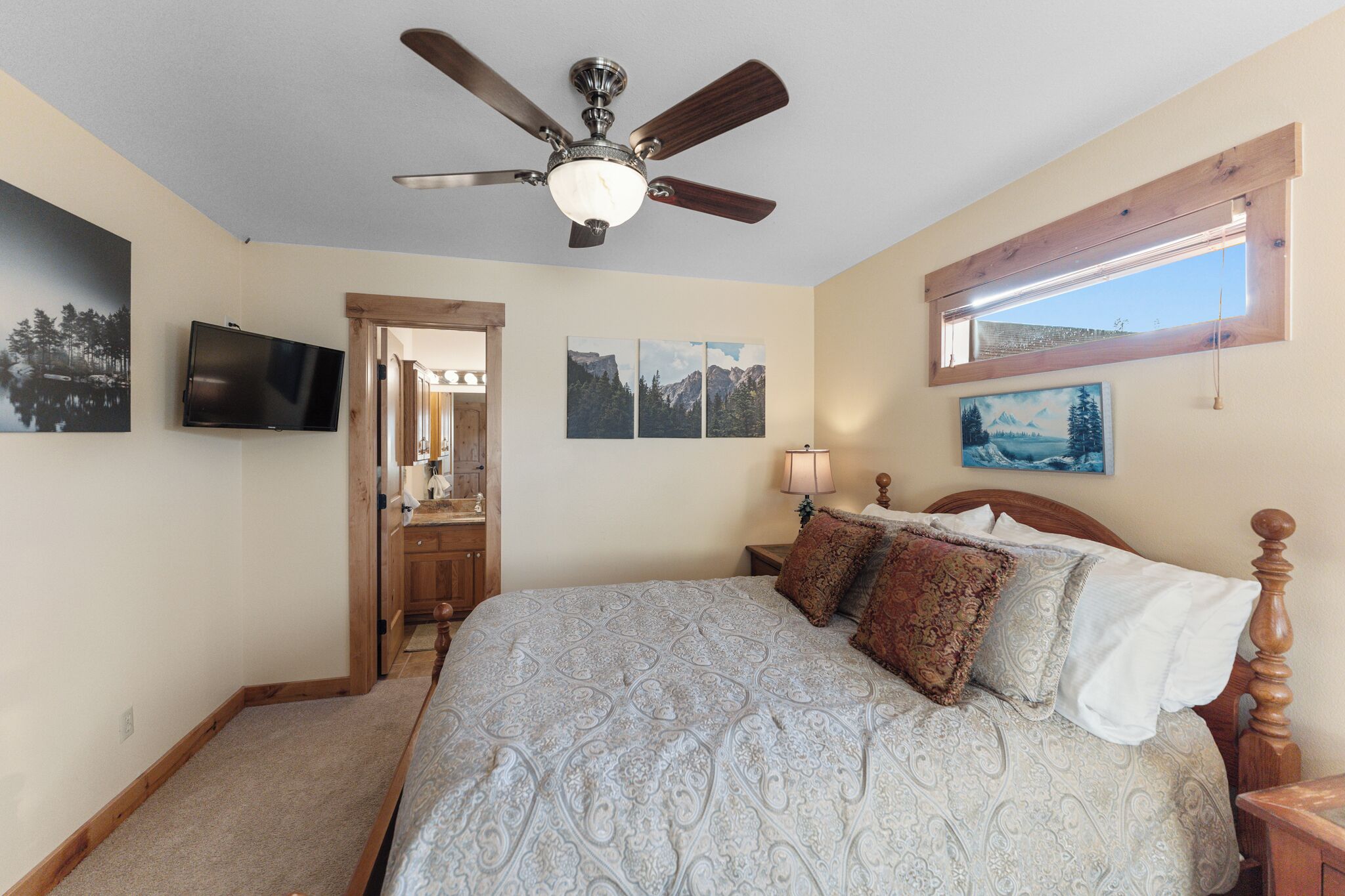 A bedroom with a bed, a ceiling fan, a TV, and a window with a view.