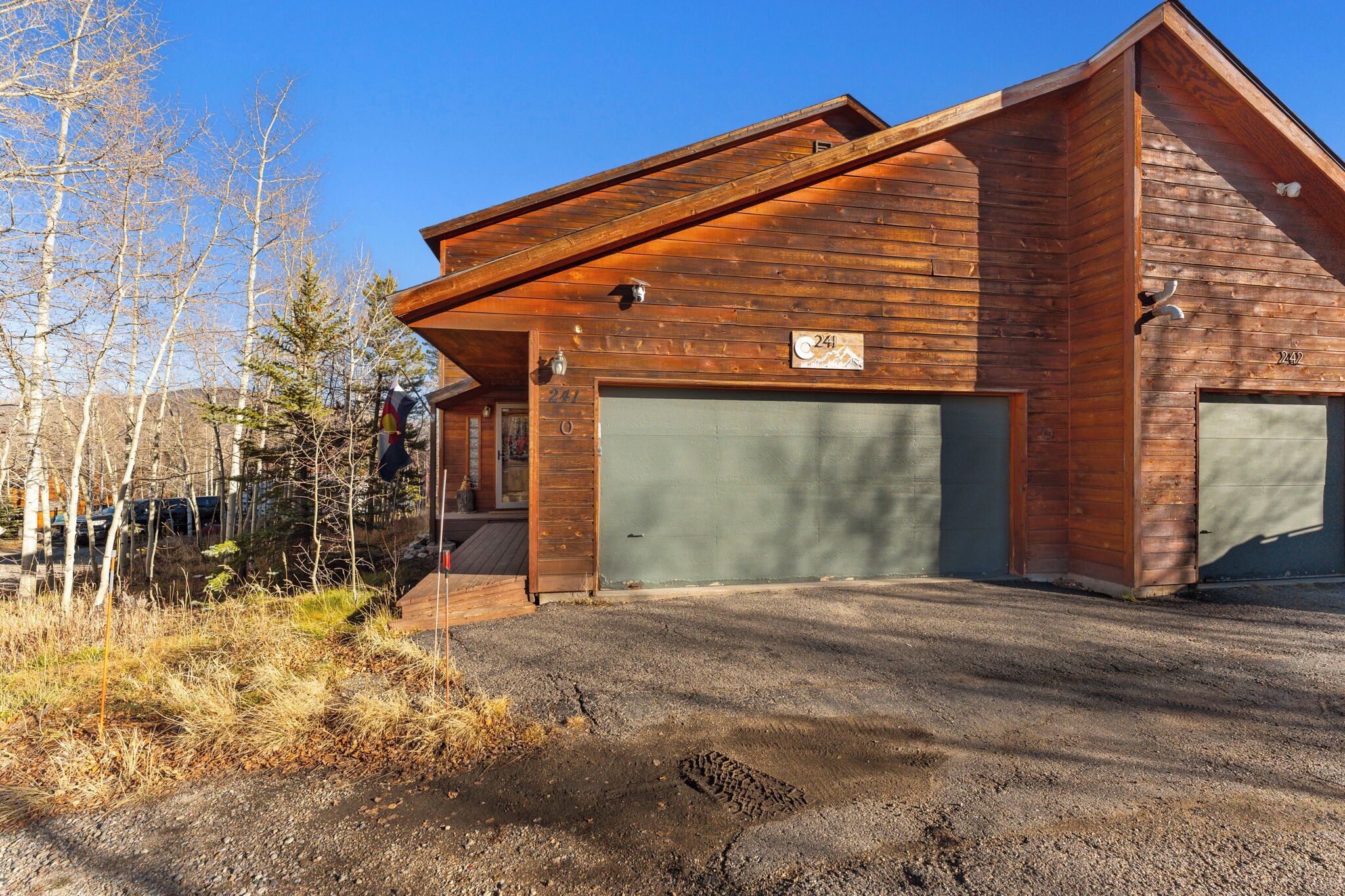 A wooden cabin with a garage, surrounded by trees and a clear sky.