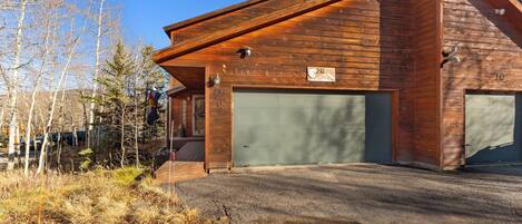 A wooden cabin with a garage, surrounded by trees and a clear sky.