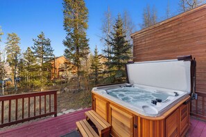 Un bain à remous sur une terrasse en bois, avec une clôture en bois et des arbres en arrière-plan.