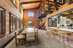 A spacious wooden cabin with a long dining table, multiple bar stools, a kitchen area, and a staircase leading to an upper level. - 0238 Wild Irishman Road by Summit County Mountain Retreats (Keystone)