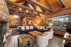 L’intérieur d’un chalet confortable, avec une cheminée, des canapés en cuir, une table basse en bois et une grande fenêtre donnant sur l’extérieur.