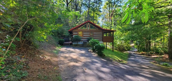A cabin with a wooden exterior, a red roof, and a driveway leading to the entrance. - Real rustic couple's getaway with hot tub (Pigeon Forge)