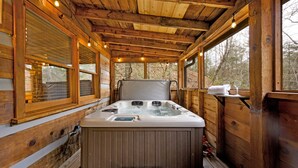 Eine Holzhütte mit Whirlpool, großen Fenstern und einer Holzterrasse.