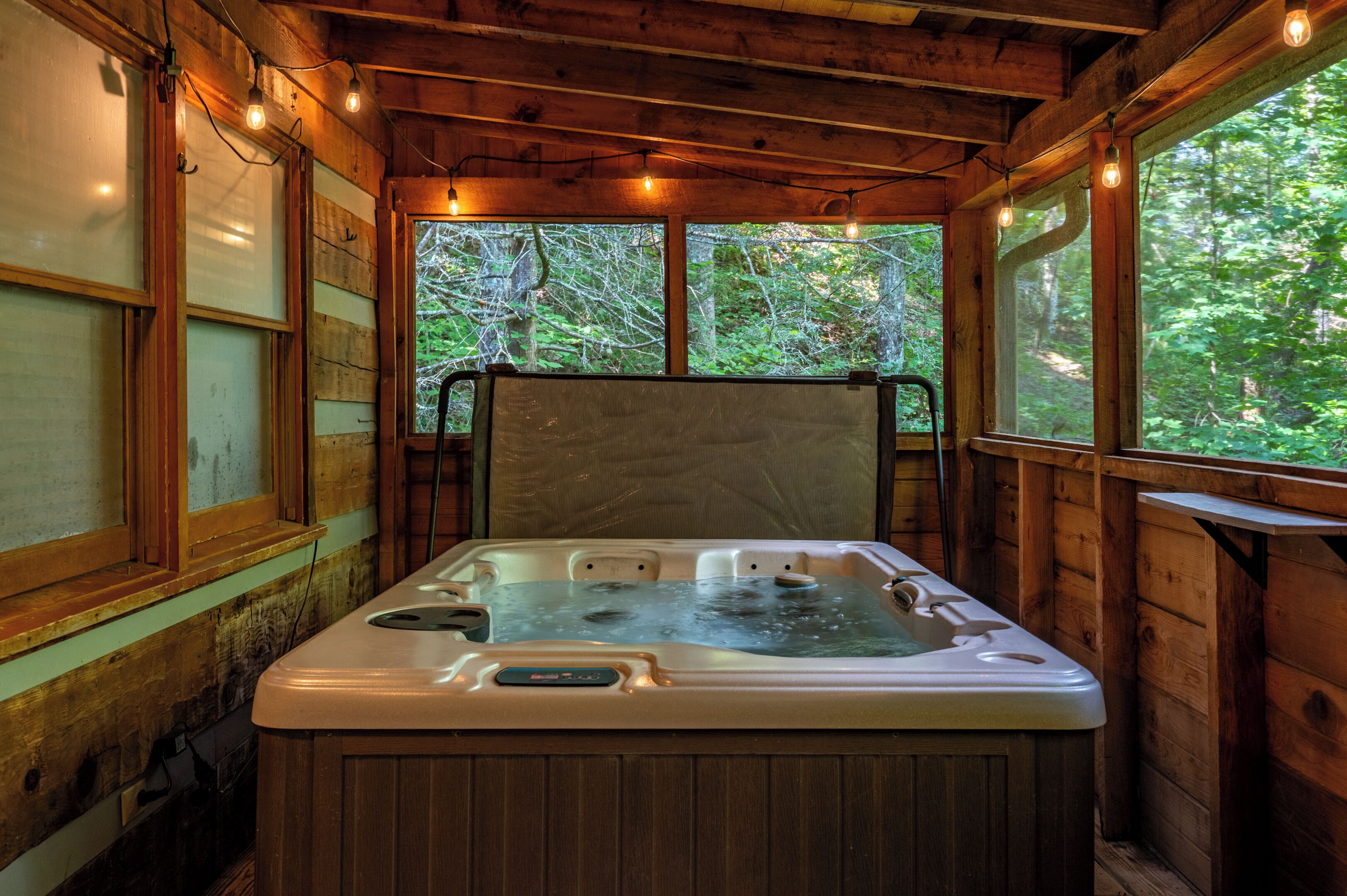 A wooden cabin with a hot tub, large windows, and string lights.