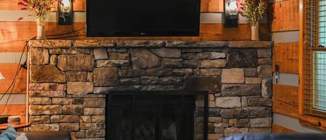 A cozy living room with a stone fireplace, a flat-screen TV mounted above it, and comfortable seating.