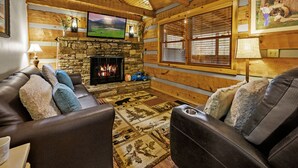 Ein gemütliches Wohnzimmer mit Kamin aus Stein, einer Ledersofa und einem darüber montierten Fernseher.