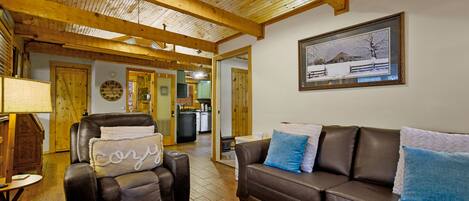 A cozy living room with a leather sofa, a recliner, and a wooden ceiling.