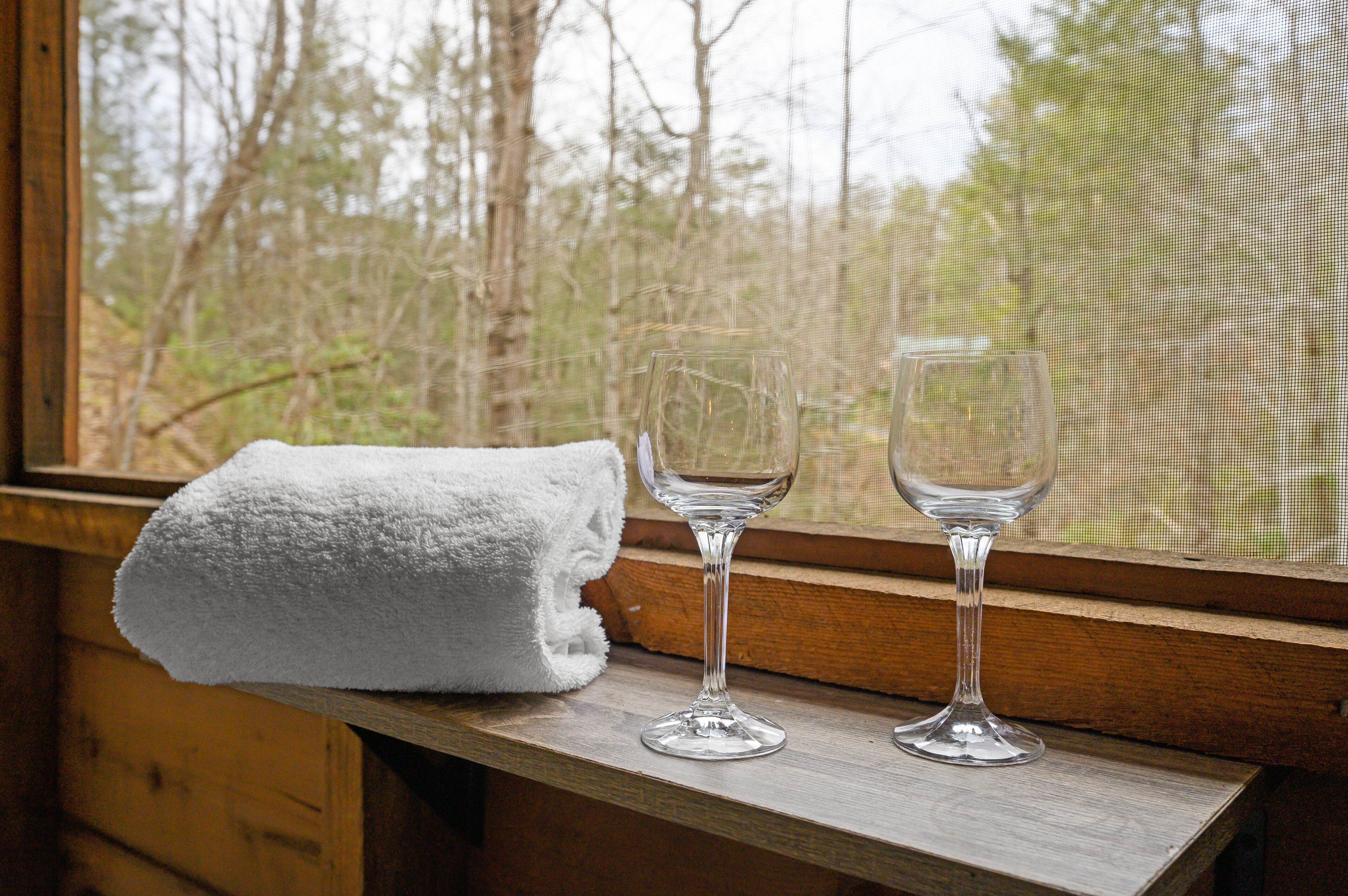 A window with a wooden ledge, a white towel, and two clear wine glasses.
