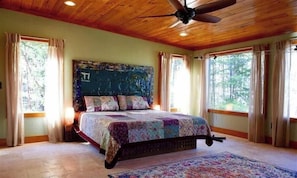 A bedroom with a large bed, wooden ceiling, and large windows.