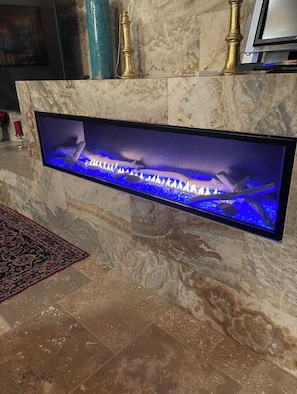 Une cheminée moderne dotée d’un téléviseur intégré, de murs en marbre et d’un tapis décoratif.