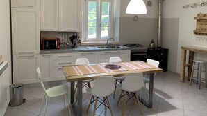 Una cocina moderna con armarios blancos, una mesa de comedor con sillas, un ventanal y una lámpara colgante.