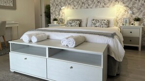 Une chambre à coucher avec un lit, des tables de chevet, un bureau et une grande commode blanche.