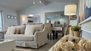 Un salon moderne avec un canapé beige, une table basse blanche et un coin repas à l’arrière-plan.