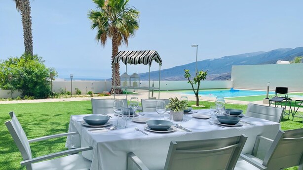 Une table à manger installée à l’extérieur, offrant une vue sur une piscine et des montagnes.