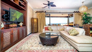 Ein geräumiges Wohnzimmer mit einer großen Couch, einem Glastisch, einem Fernseher und Blick aufs Meer.