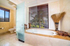 A bathroom with a bathtub, toilet, and a window with blinds.