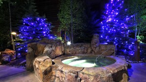 Un jacuzzi rodeado de formaciones rocosas y árboles iluminados.