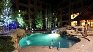 Un área de piscina interior con borde de piedra, árboles y un edificio al fondo.