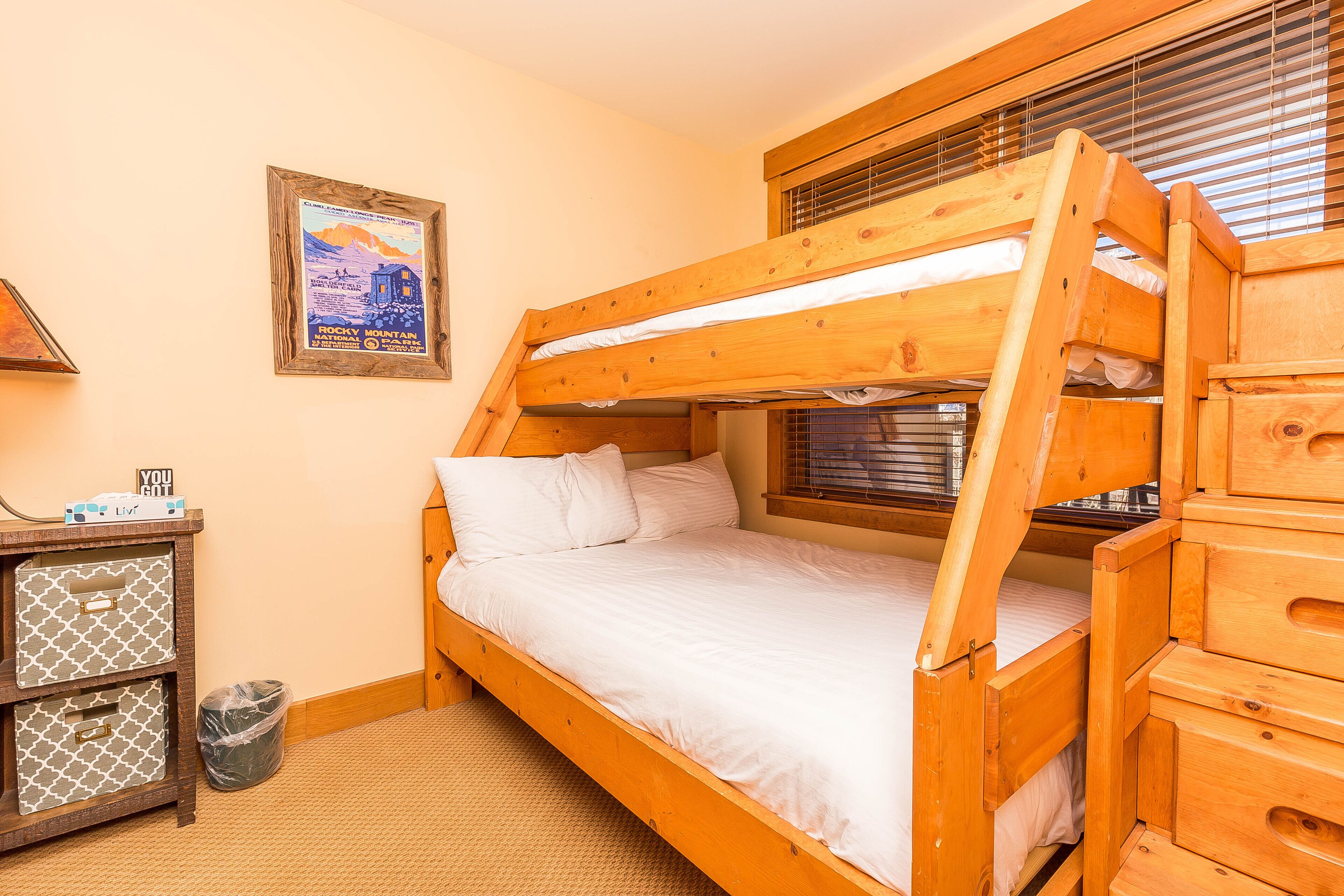 A bunk bed with a wooden frame, a small desk with a lamp, and a framed picture on the wall.
